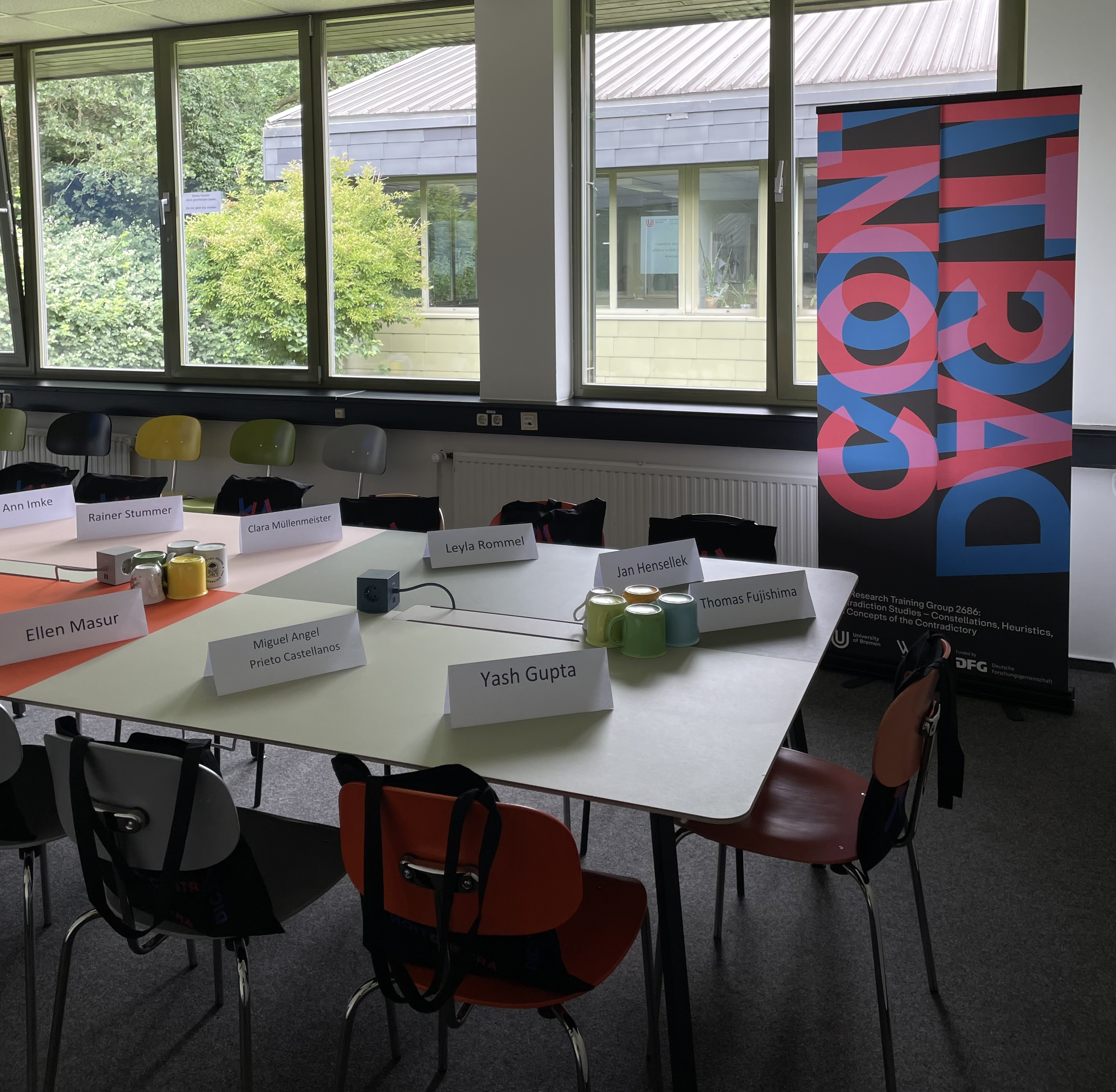 The table can be seen in an office room of the RTG Contradiction Studies. On the table are paper signs with the names of the new doctoral students and welcome bags on the chairs.
