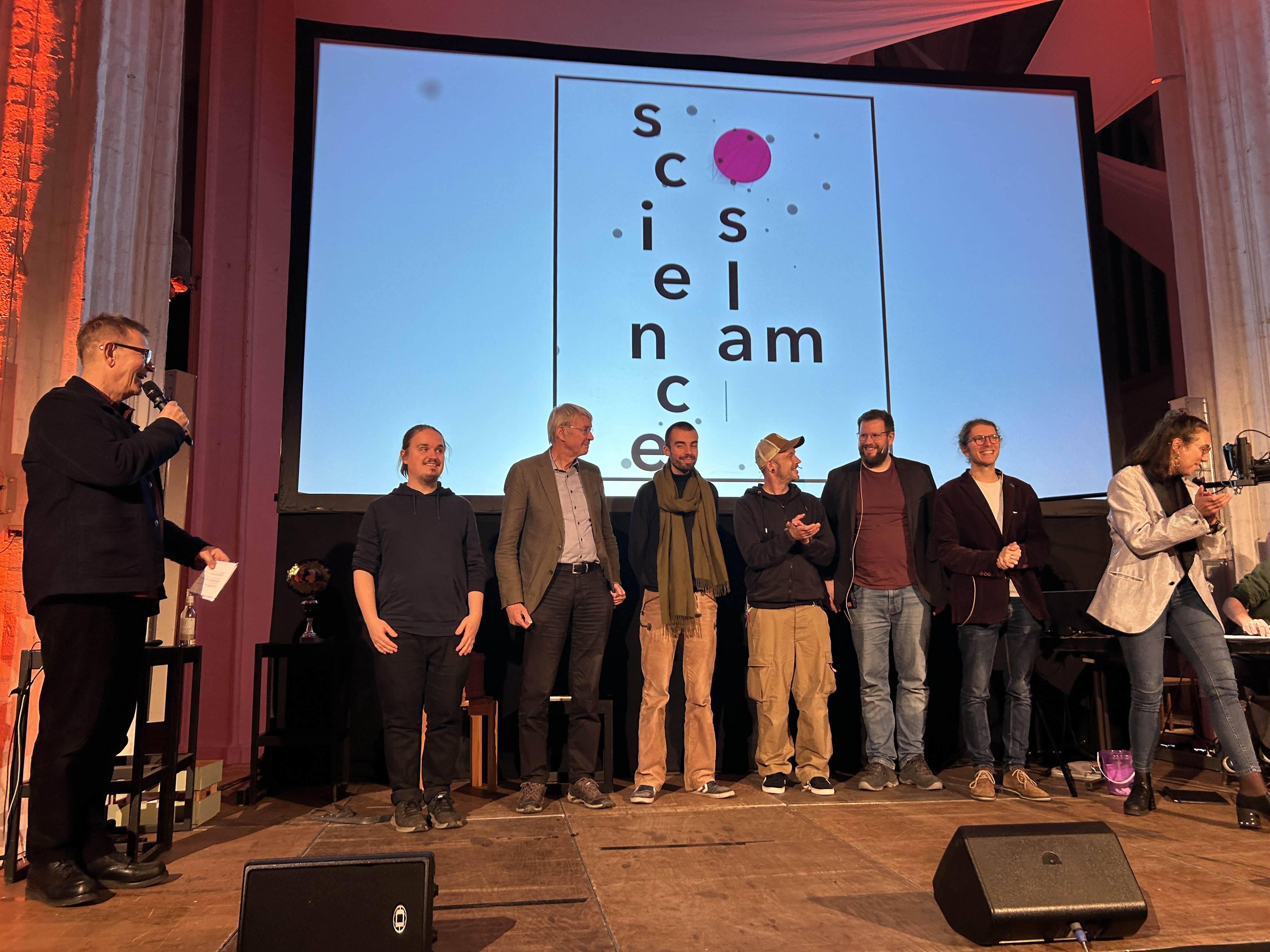 Eine Gruppe von Menschen stehen auf einer Bühne beim Science Slam in Lübeck.